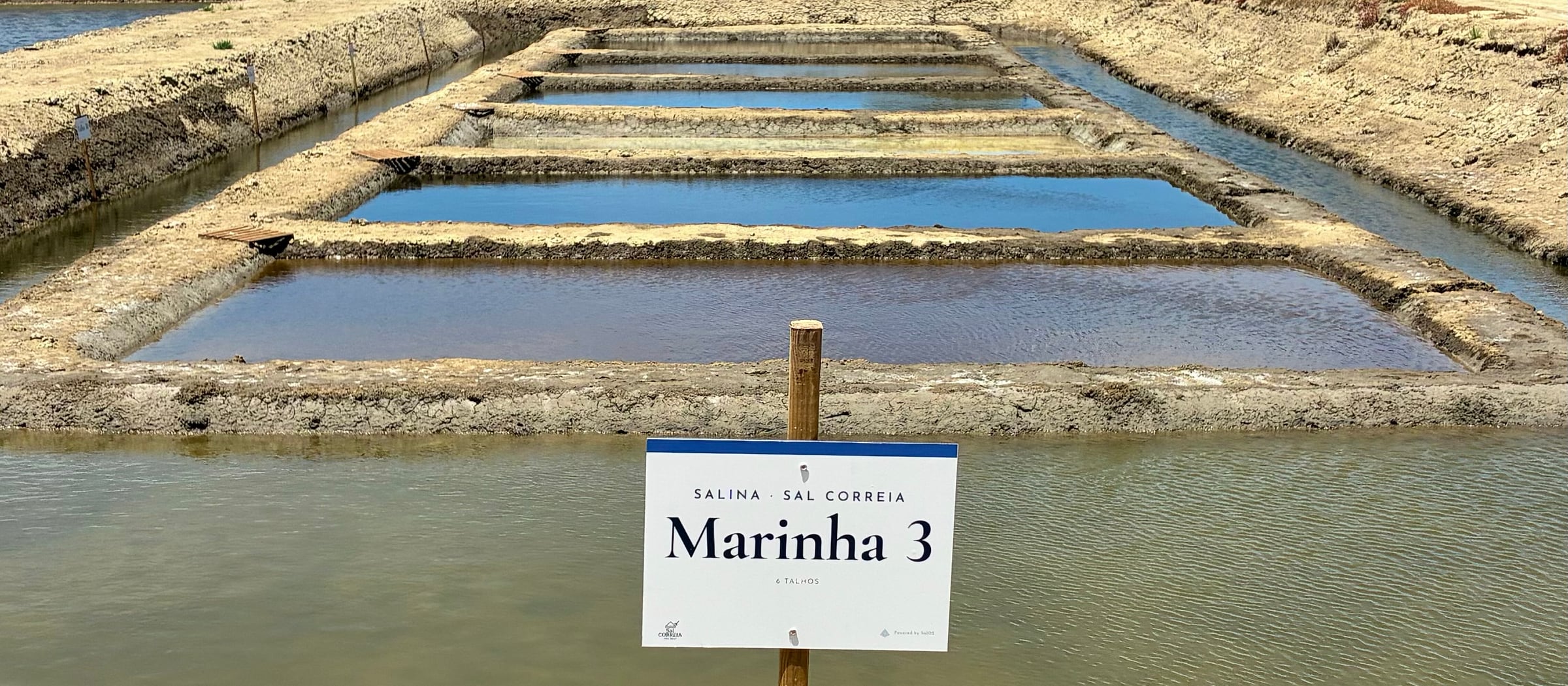 A wooden post marking Marinha 3 at the Sal Correia salt pans, with the rebuilt crystallisation talhos behind it.